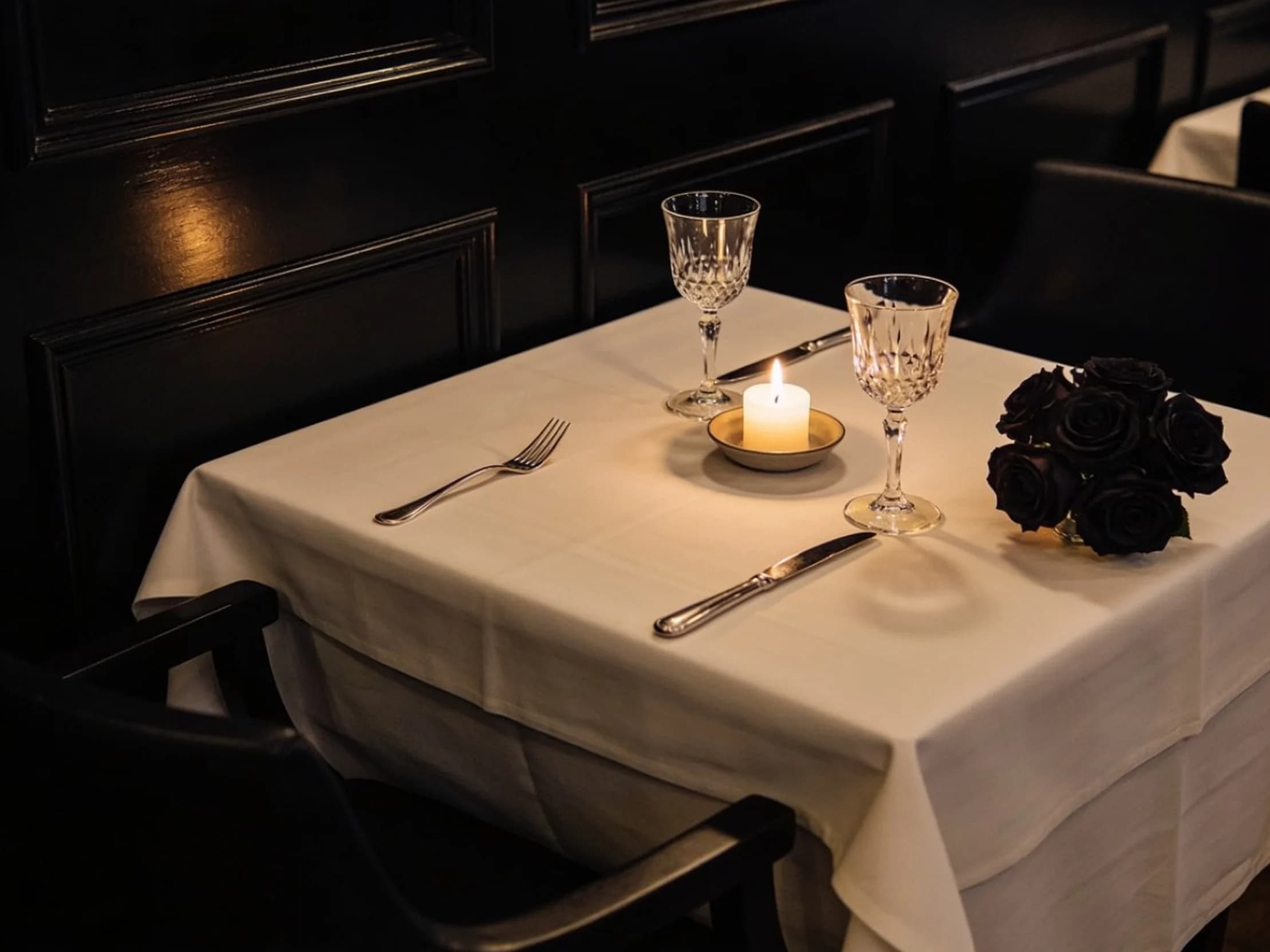 A restaurant table for two laid with white linen, crystal glasses and a single candle.