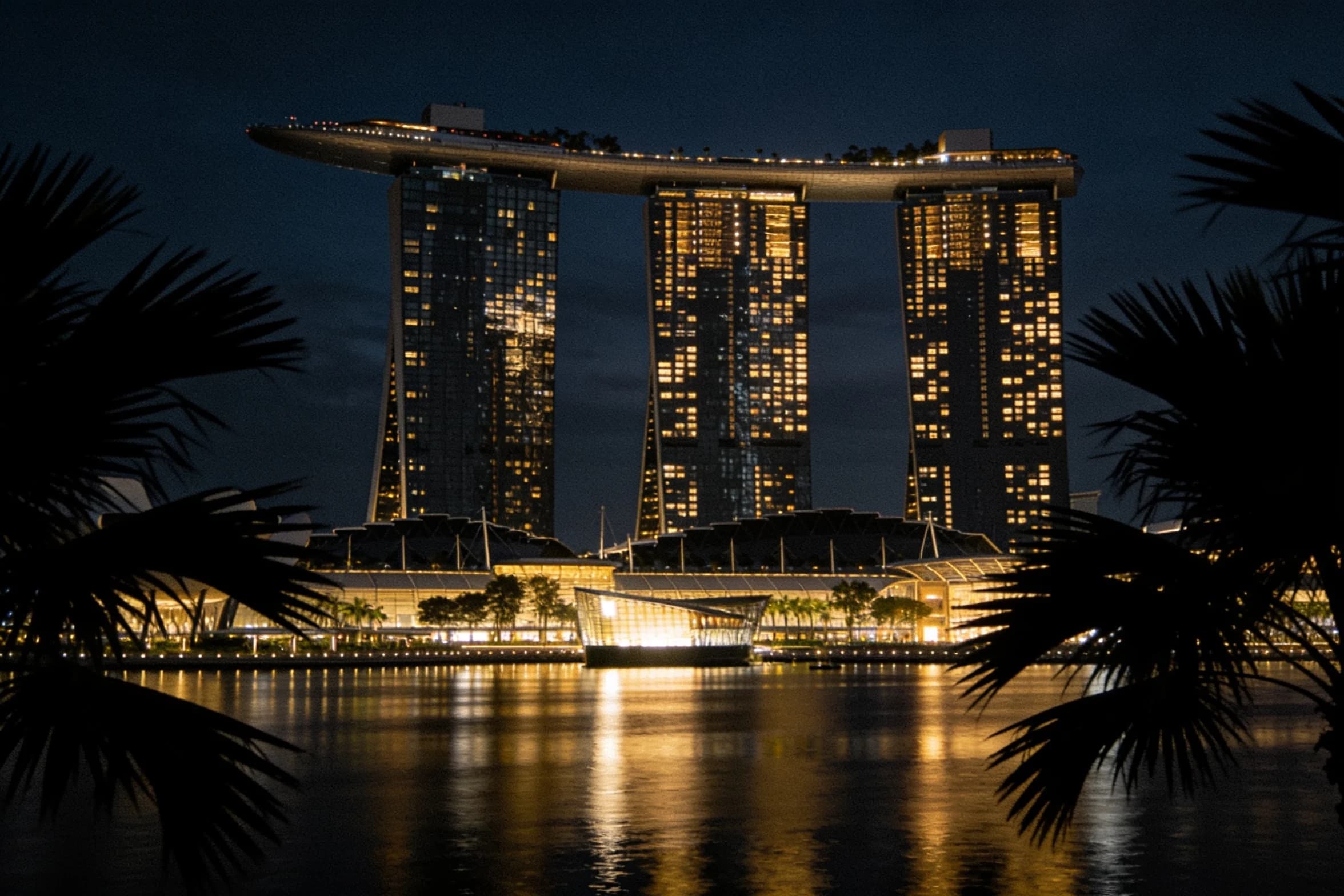 The Marina Bay waterfront at night, towers mirrored in dark, still water.