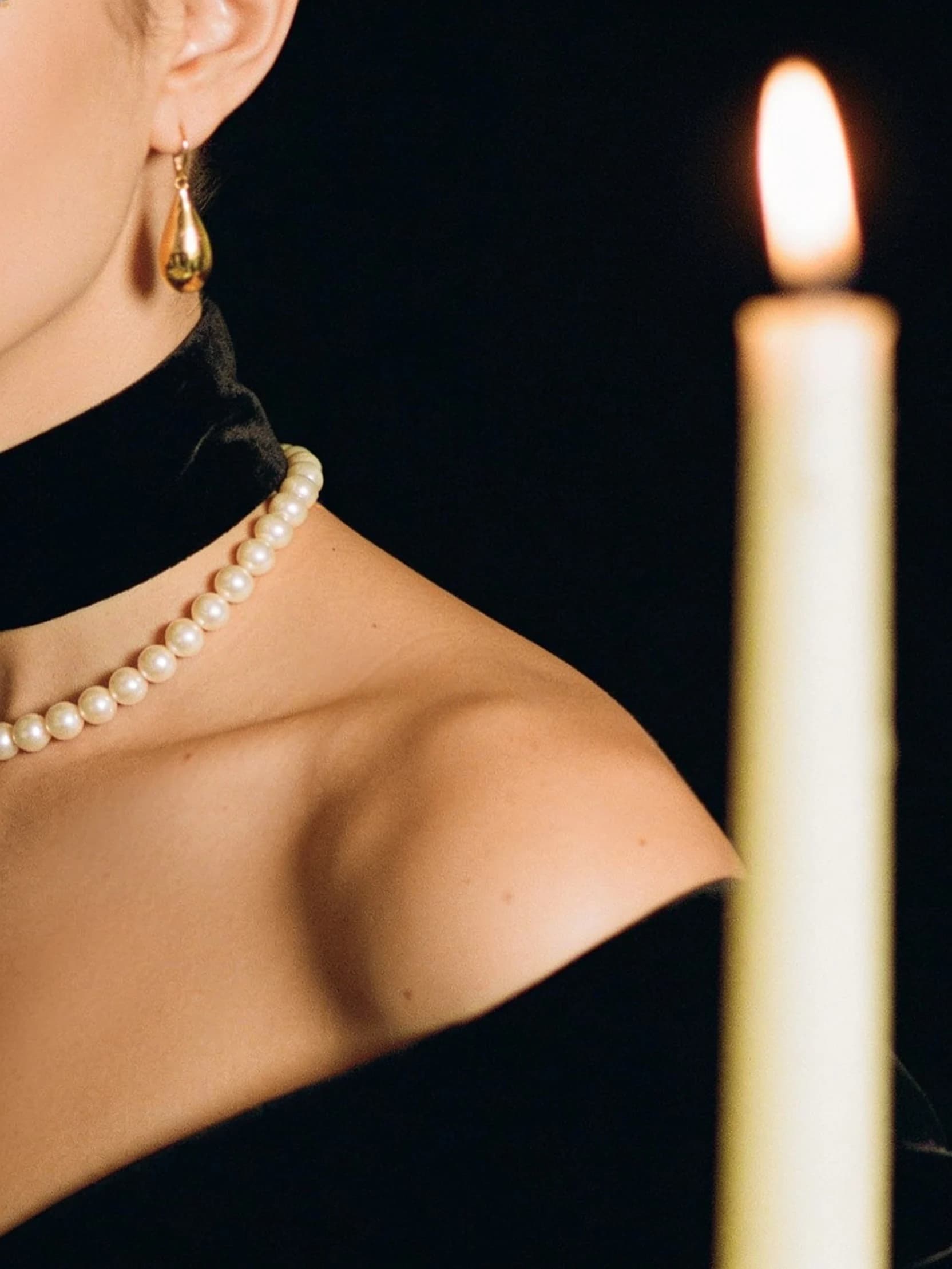 A close detail of Aiko in a black velvet evening dress with a strand of pearls, cropped above the shoulders.