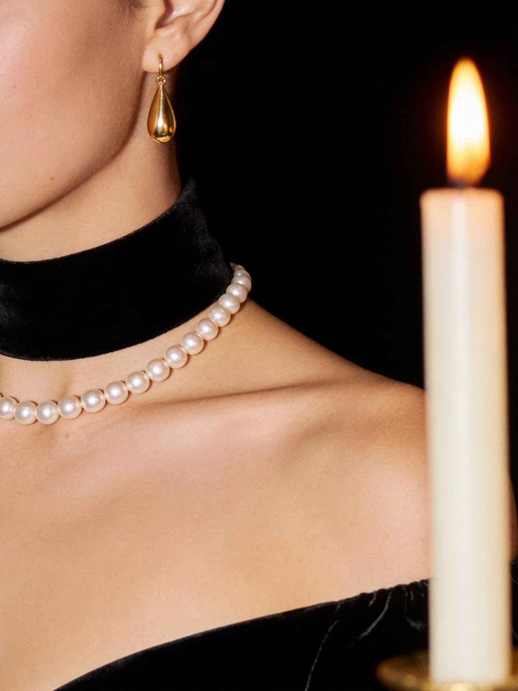 A close detail of Isabelle in a black velvet evening dress with a strand of pearls, cropped above the shoulders.