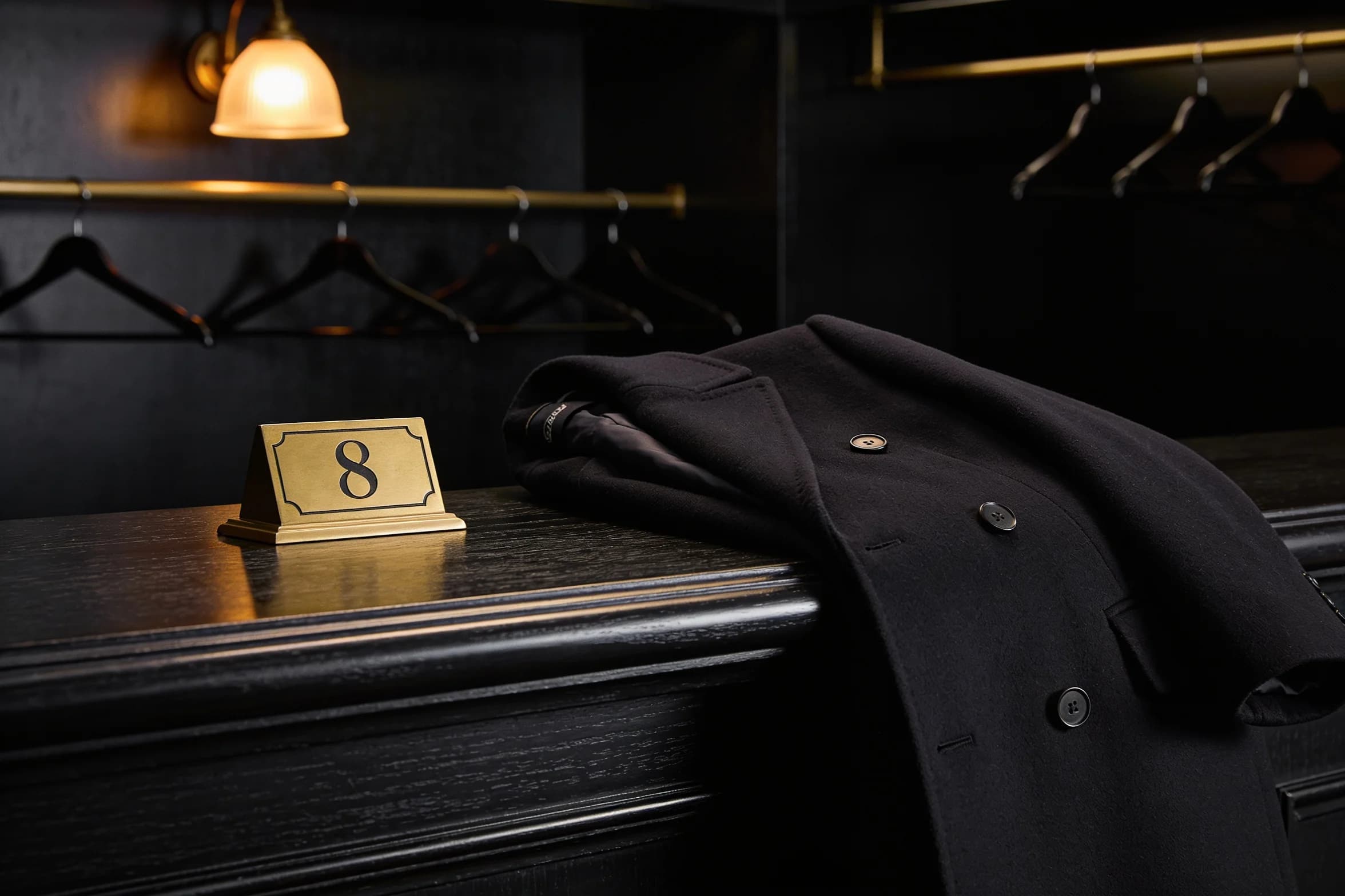 A cloakroom counter at night, one numbered brass tag left on the wood beside a folded coat.