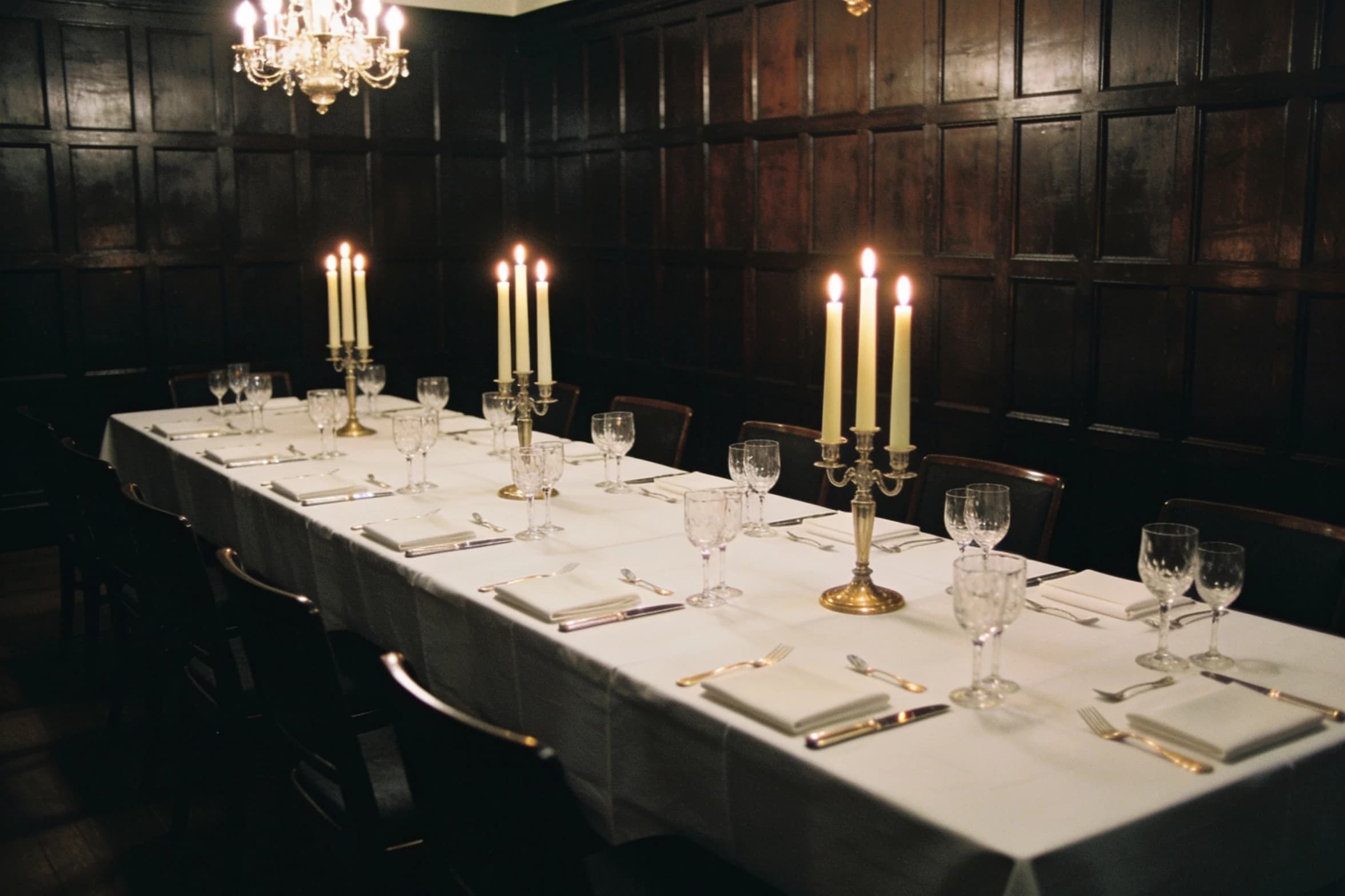 A long dinner table laid for twelve in a panelled private room, chairs pushed back before service.